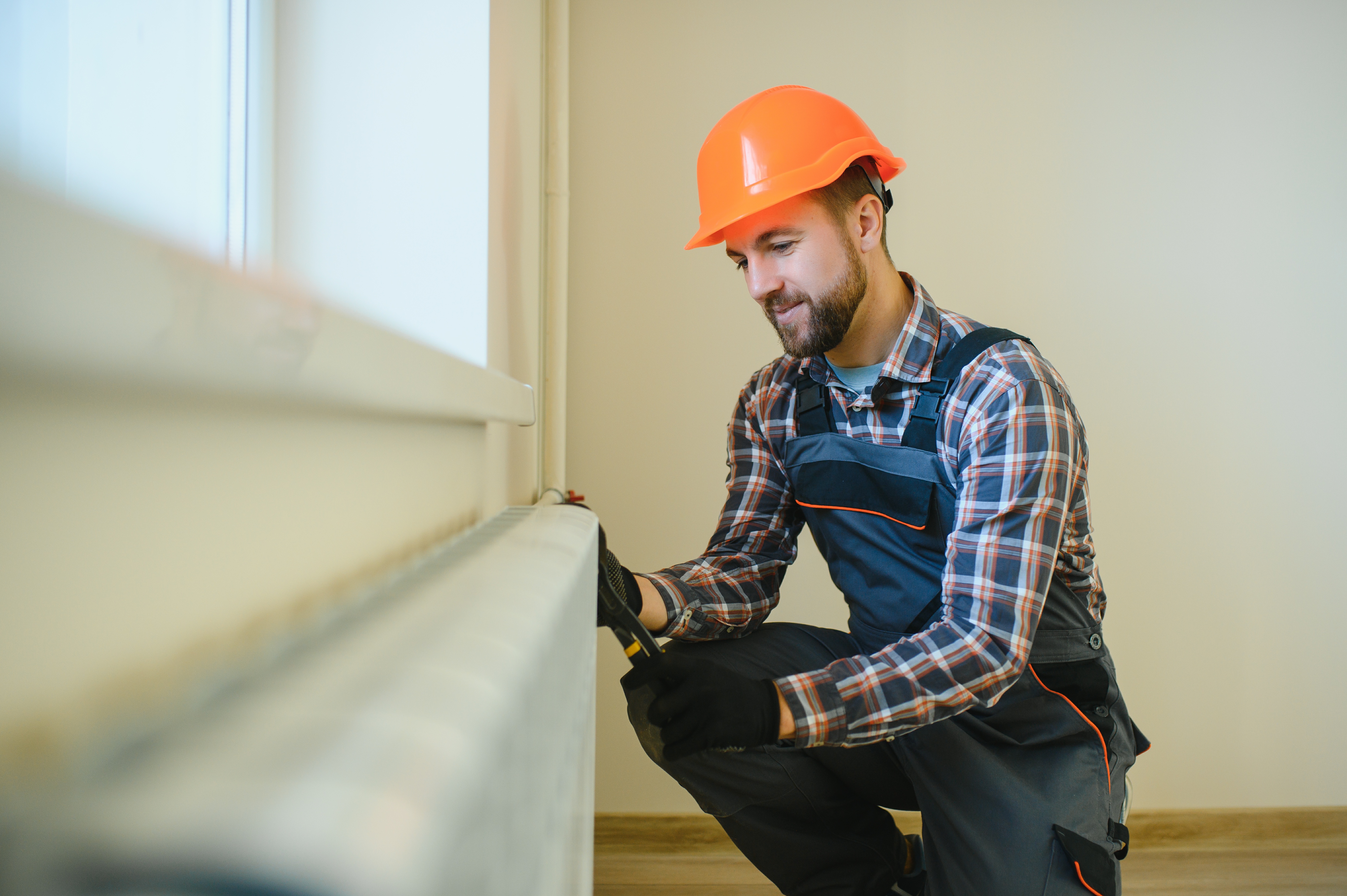 Technicien réparant un radiateur avec casque orange.