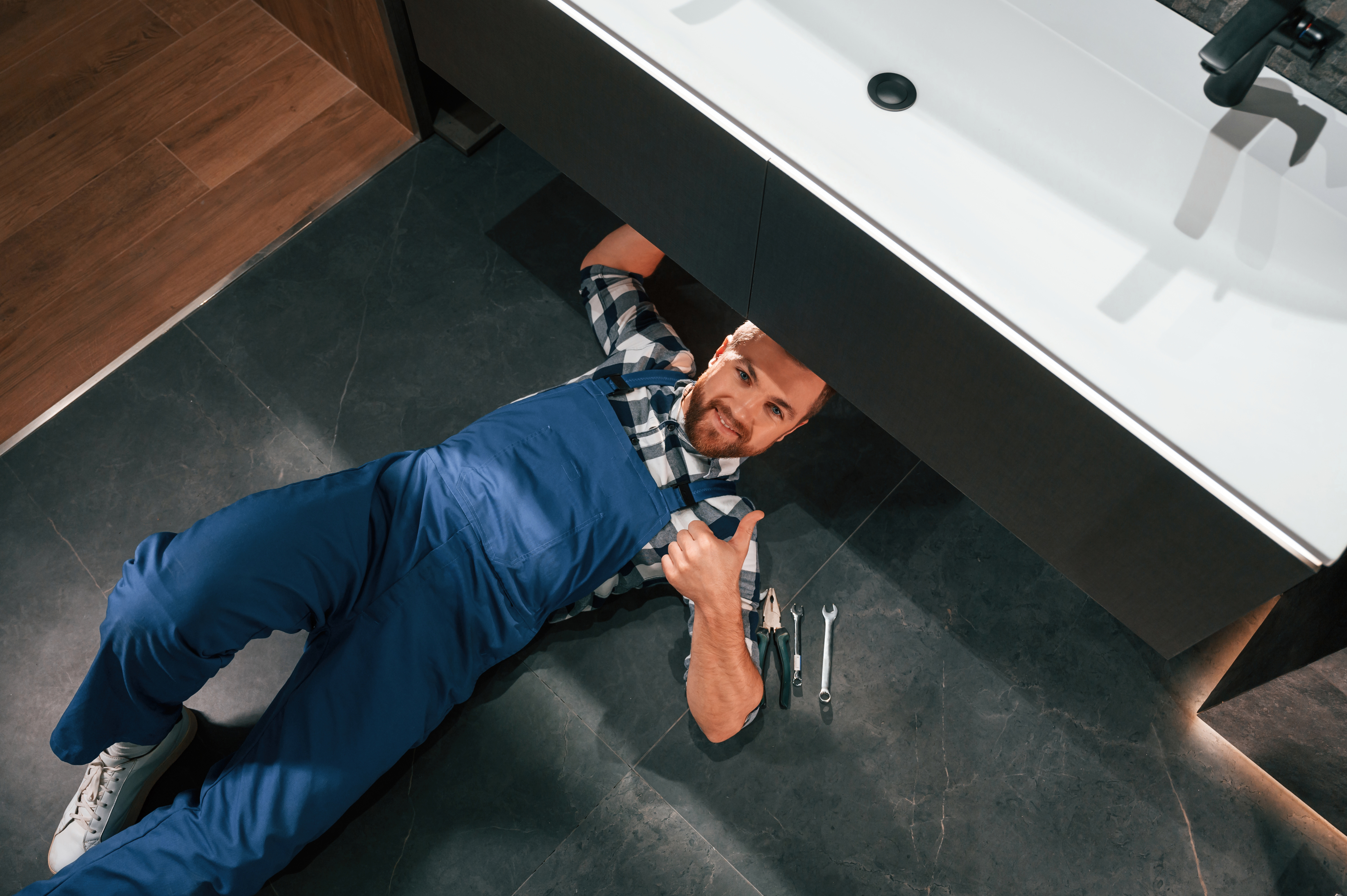 Plombier travaillant sous un évier avec outils.
